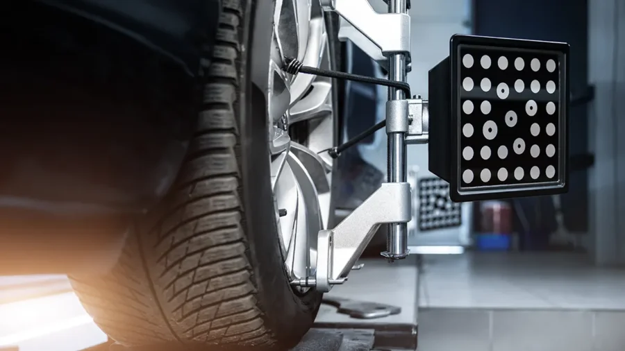 Un appareil de mesure d'alignement est fixé à une roue de voiture, montrant des pneus et des équipements de garage en arrière-plan.