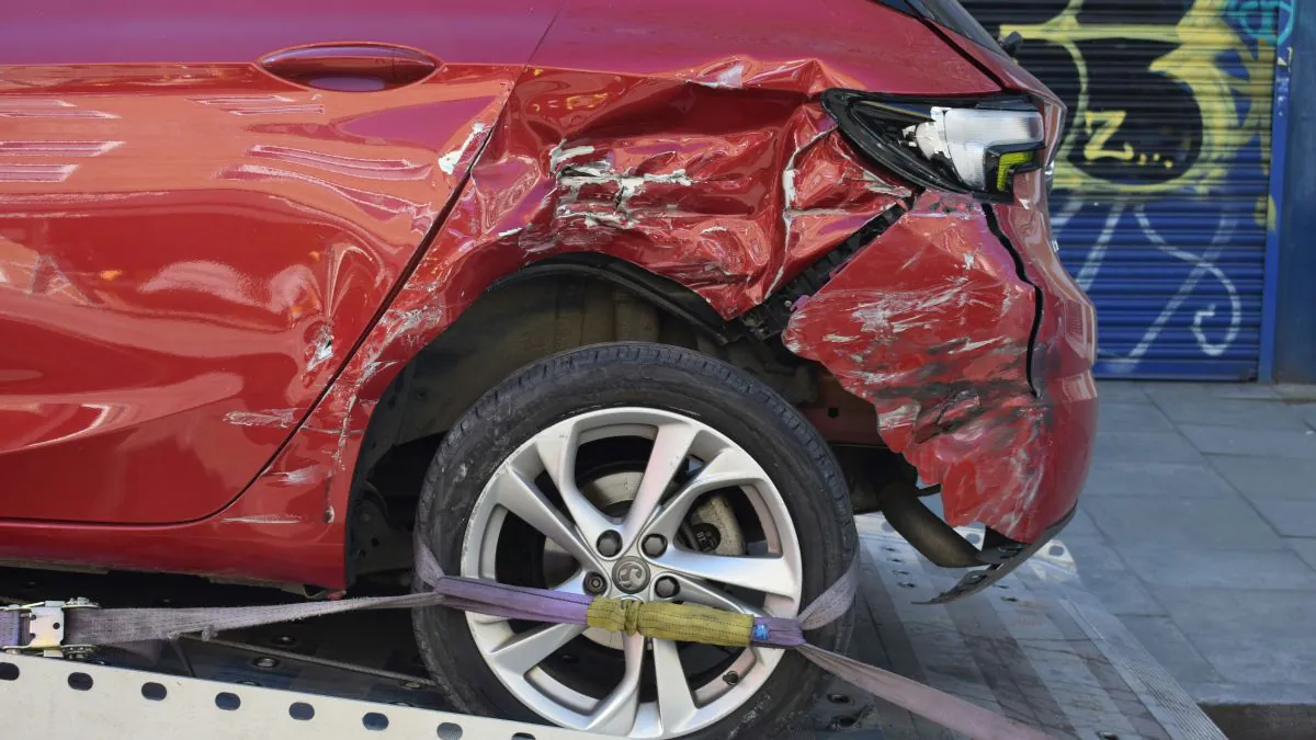 Véhicule rouge endommagé sur un plateau de remorquage, avec des éraflures visibles sur la carrosserie et une roue arrière immobilisée.
