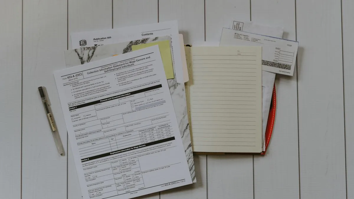 Documents administratifs et un carnet de notes disposés sur une surface claire, accompagnés d'un stylo et de feuilles.